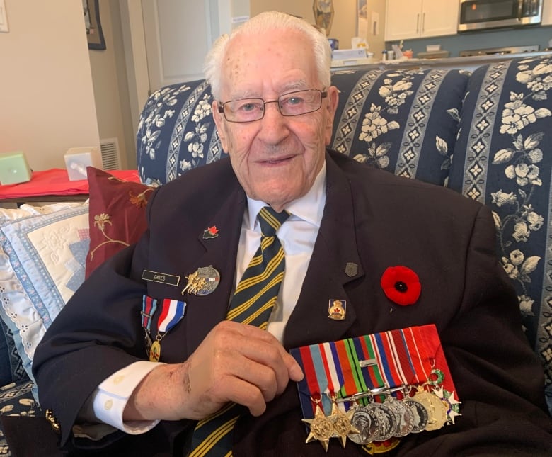 Man with gray hair, white button-up shirt and tie and navy blazer show his war medals pinned to his jacket. 