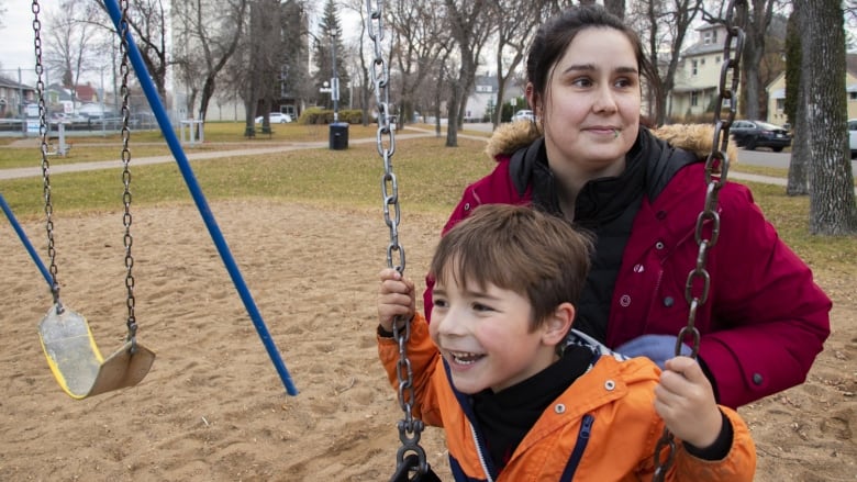 A mom pushes her son on a swing.