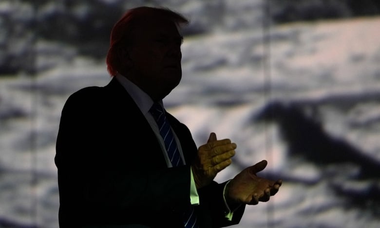 A shadowy silhouette of a man is mid-clap. Behind him, a dappled grey backdrop is shown. 