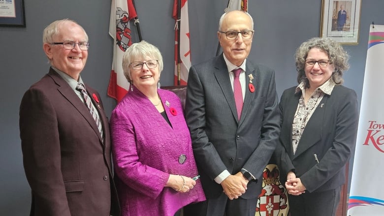 Four people stand in a row smiling.