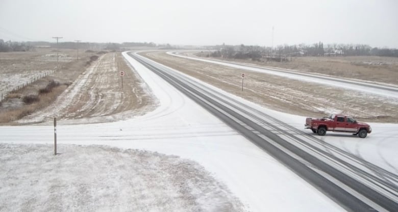 A highway with snow and a red truck driving.