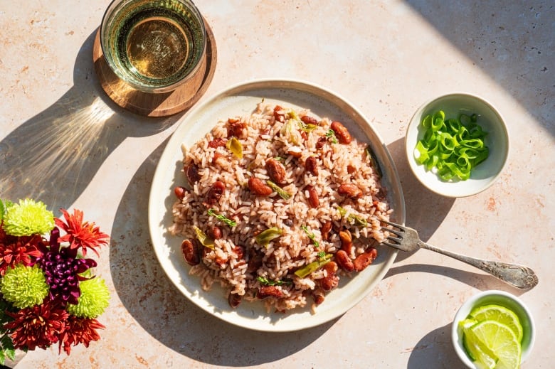 Overhead shot of a plate of rice and peas with bowls of sliced limes and green onions next to it. 