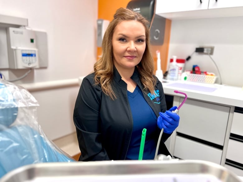 A woman sits on a chair holding a tool used to suction excess saliva from people's mouths during dental appointments. 