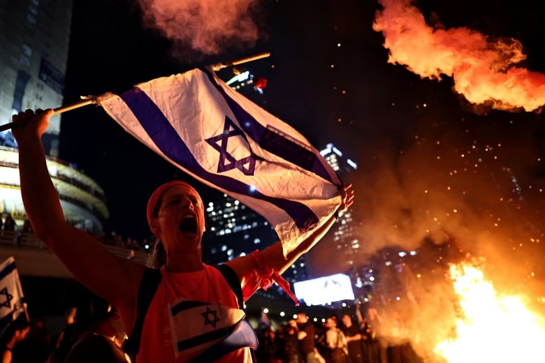 A person holds an Israeli flag as people demonstrate after Israeli Prime Minister Benjamin Netanyahu sacked his defense minister, Yoav Gallant, citing lack of trust, in Tel Aviv, Israel November 5, 2024. REUTERS/Thomas Peter