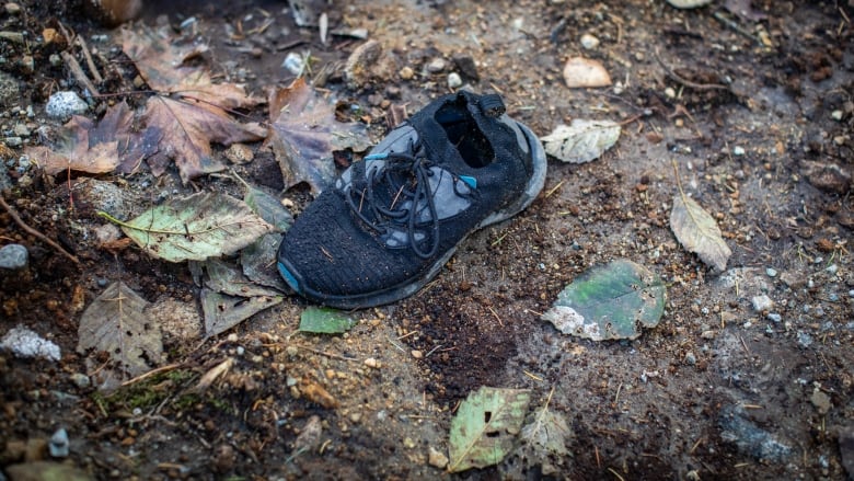 A shoe sits among leaves and debris on muddy ground.