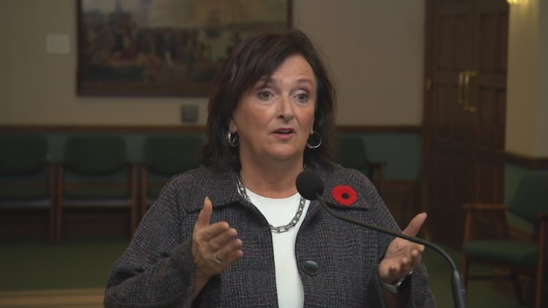 A woman gestures while standing behind a microphone.