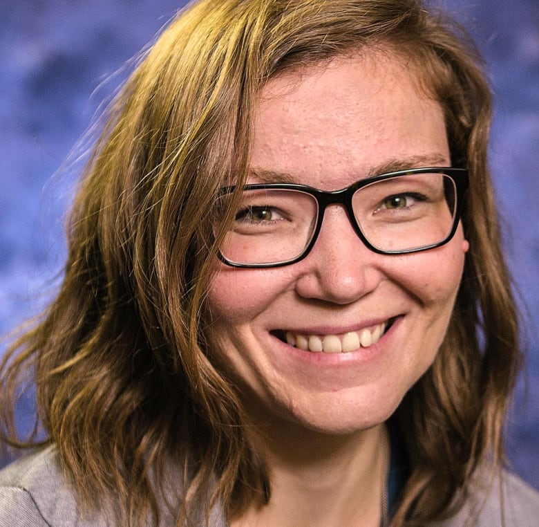 Woman with wavy brown hair and black glasses smiling.