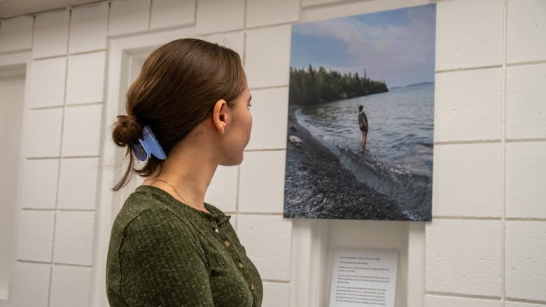 A person is seen from the side, staring at a photo on the wall.