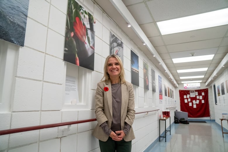 A person is seen standing in a hallway of photographs. They are smiling.