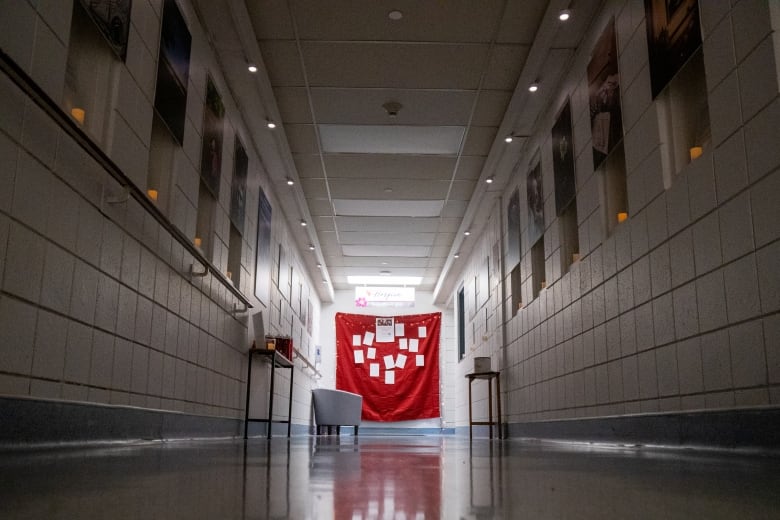 A long, dark hallway lit by candles and a bright light at the end of the hallway. Photos are seen on the walls.