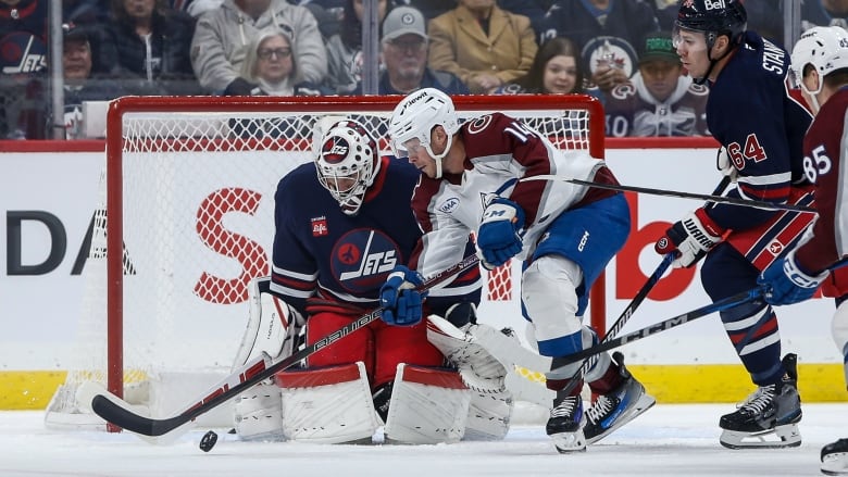 A goaltender in blue watches a player in white with the puck.