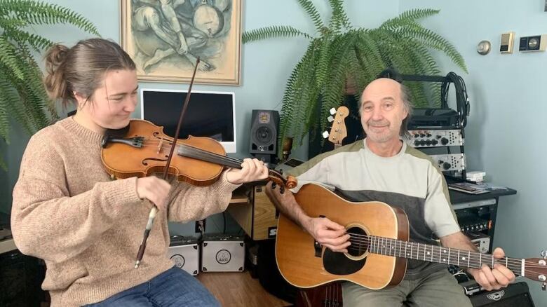 A woman plays fiddle and an older man holds a guitar.