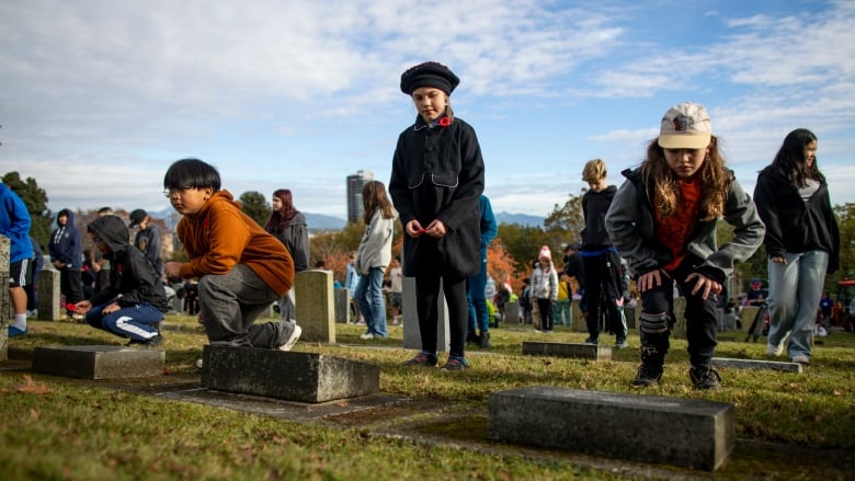 A girl stands holding a poppy and looks at a gravestone.