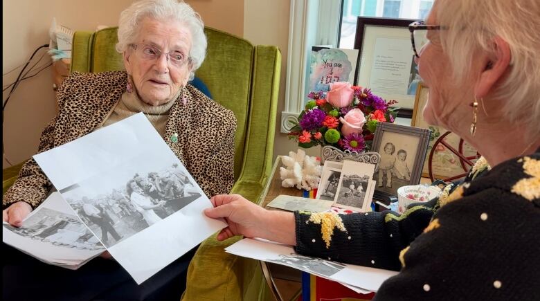 Two older women sit looking at photos.