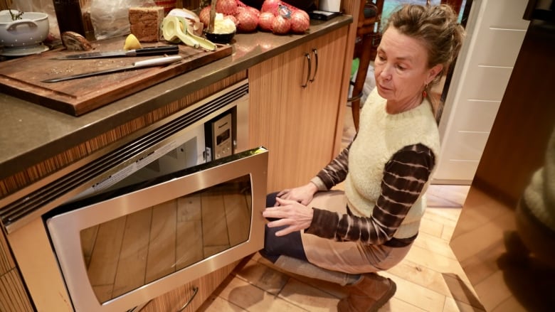 A woman crouches down to look at her microwave installed on a lower shelf.