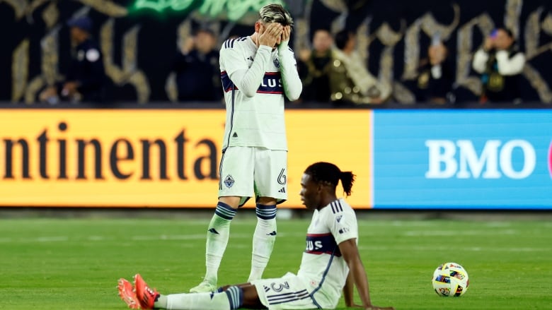 A soccer player holds his head in his hands, dejected, as his teammate sits on the turf.