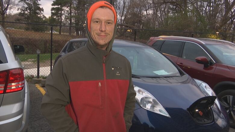 A man wearing wind-breaking atire stands in front of a blue electric vehicle.