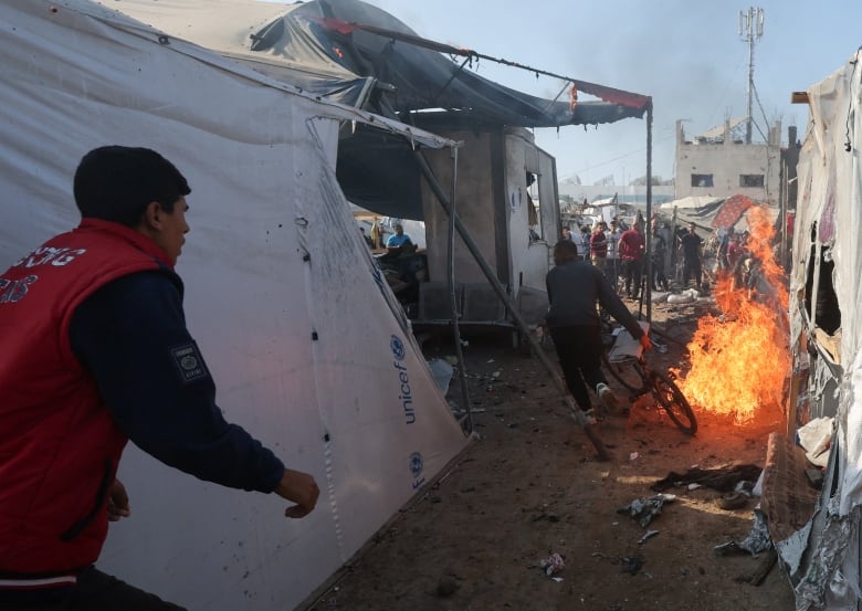 A person with a bike runs away from a fire burning in between tents at a refugee camp.