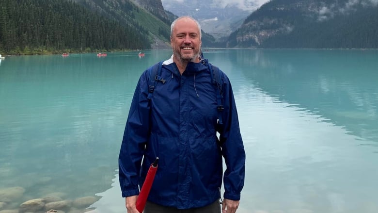 A man smile as he stands in front of a lake and mountains.