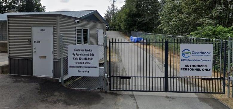 An entrance to a water utility, with a security office and a sign reading 'Clearbrook Waterworks District' on a gate.