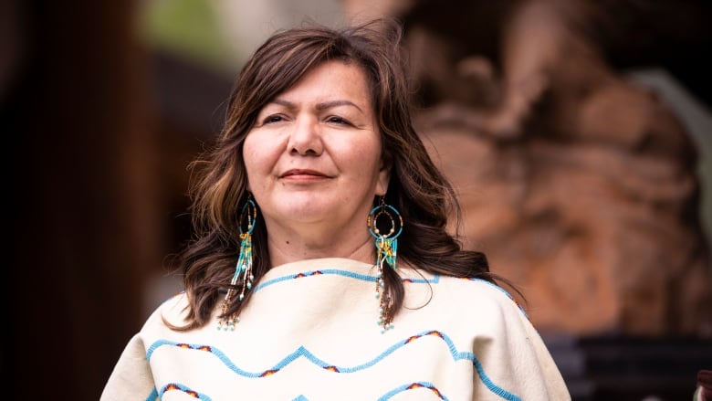 An Indigenous woman wearing a white top looks off to her right.