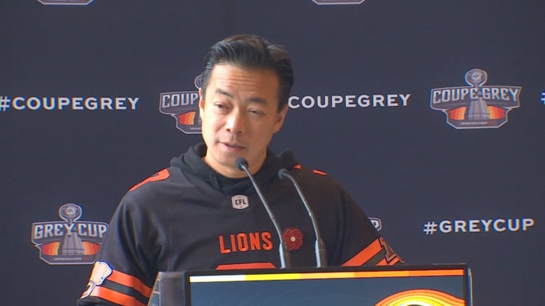 A man donning a hoodie speaks on the microphone from a podium.