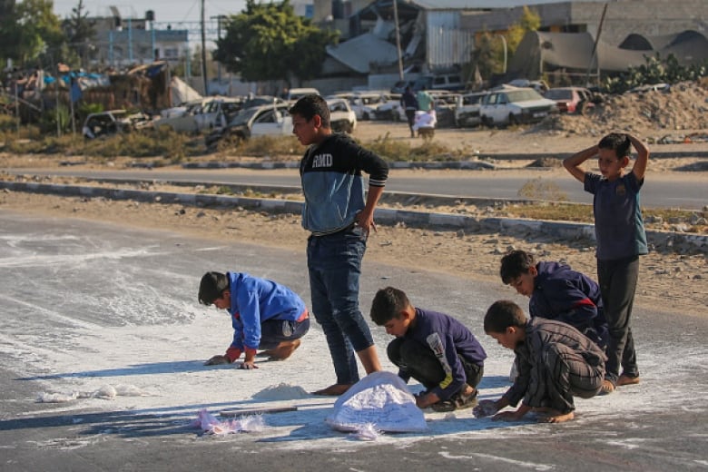 A group of boys scrape flour off a road.