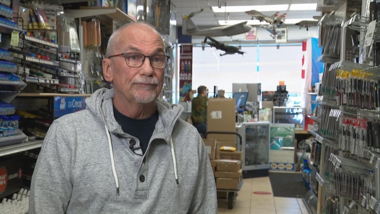 A man stands in a store with shelves and several toy model airplanes shown in the background behind him.