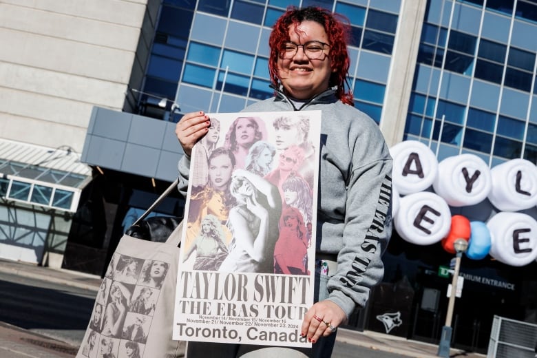 Holding a canvas bag on one shouldner, a woman shows off a poster that reads: Taylor Swift The Eras Tour, Toronto, Canada, outside Rogers Centre.