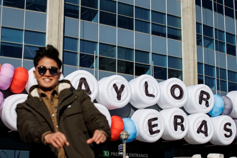 A person moving to a beat, in front of the giant friendship bracelet sign outside Rogers Centre that reads: Taylor Swift The Eras Tour.