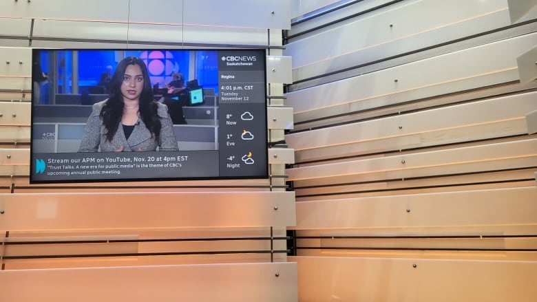 A TV hangs from the ceiling. On it a South Asian reporter with long brown hair and a blazer reads the news. The wall behind the TV is shades of orange