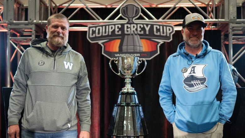 Two men stand beside a trophy.