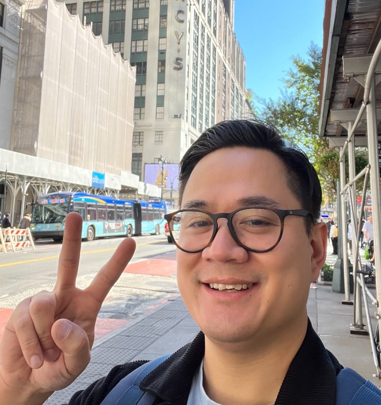 Jason Loo (early 30s, short black hair, glasses) flashes a peace sign.