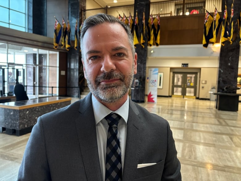 A man wearing a grey suit stands in a large lobby.