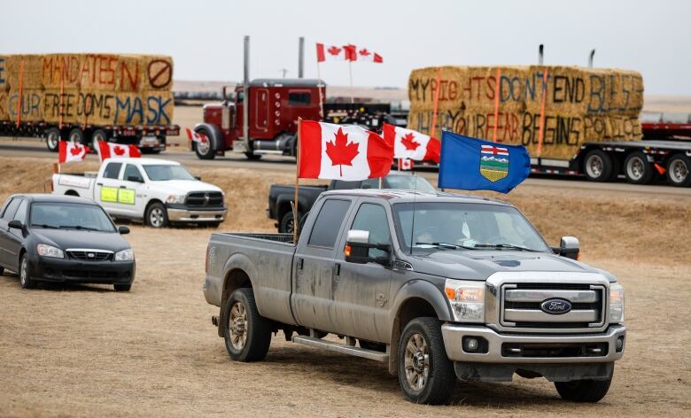 A pick-up truck with Canada and Alberta flags is parked on the median of the highway with haybales behind it.