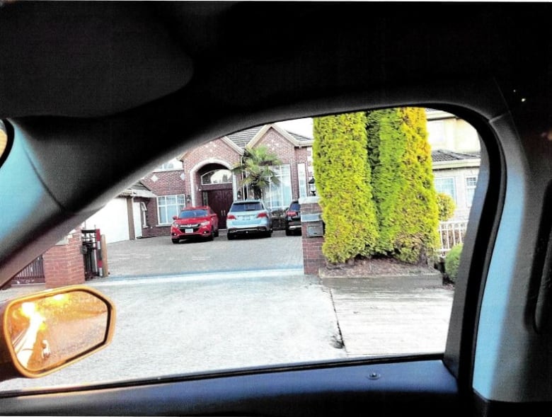 A view out of a car's side window shows the driveway of a palatial residence with three cars parked in front.