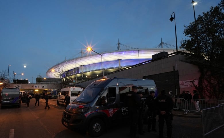 Police officers are seen outside a large stadium at dusk.