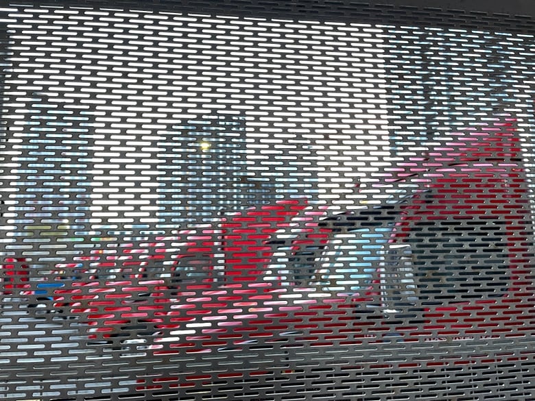 A metal screen with small openings that looks into a parking lot with many red transport trucks.