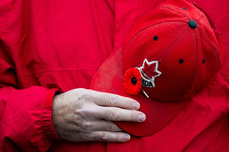 A person holds a ball cap with a poppy attached to it during the playing of the bugle call Last Post during a Remembrance Day commemorative event at the National Military Cemetery at Beechwood Cemetery in Ottawa, on Monday, Nov. 11, 2024.