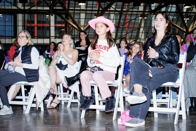 Swifties sitting in chairs and watching a costume show during Taylgate '24 at the Metro Toronto Convention Centre ahead of the first Taylor Swift Eras concert in Toronto.