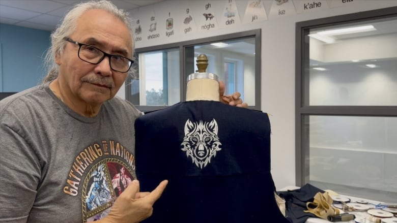 A man points to a garment embroidered in white thread with a wolf.