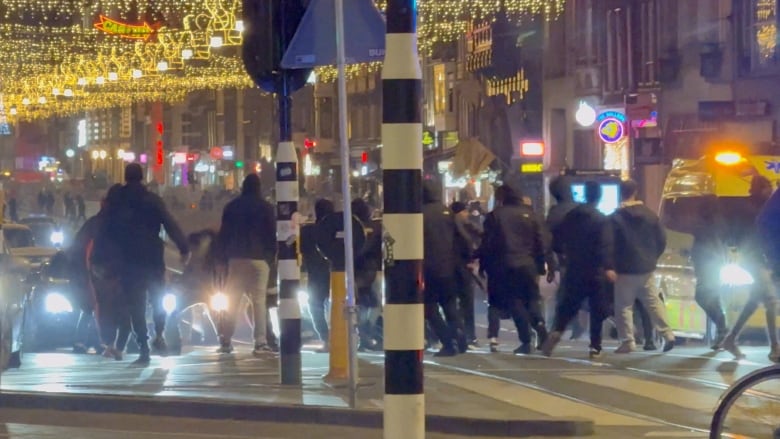 A group of men clash on a street underneath bright lights.