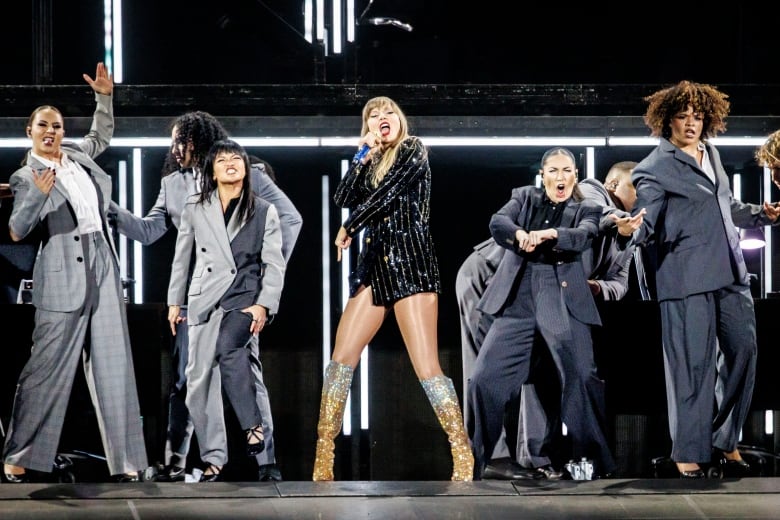 Taylor Swift on stage with her back singers and dancers, performing