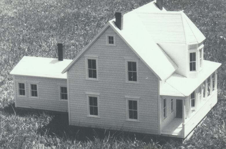 A black and white photo of a realistic-looking dollhouse on a grassy lawn.