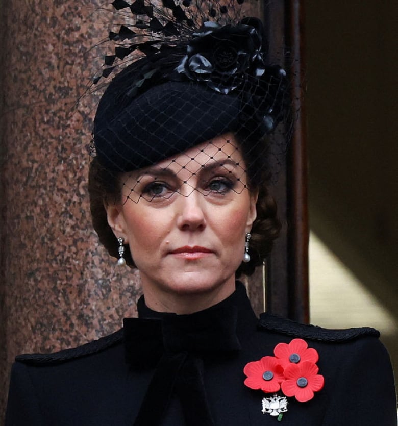 A person wearing a fascinator and a pin with three poppies near the left shoulder looks straight ahead.