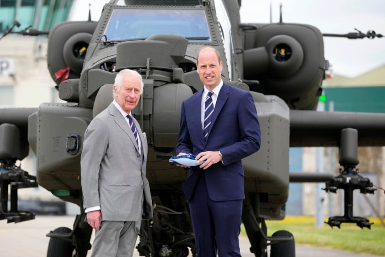 Two people stand in front of a military helicopter.