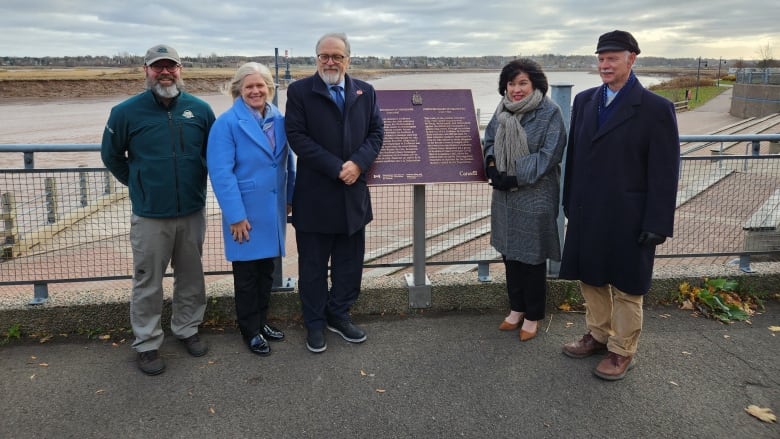 Four people stand beside a plaque in front of a river.