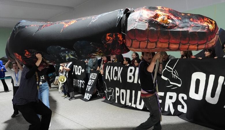 Activists carry a giant model of a red and black snake above their heads, walking in front of another big group of people holding a banner that says 