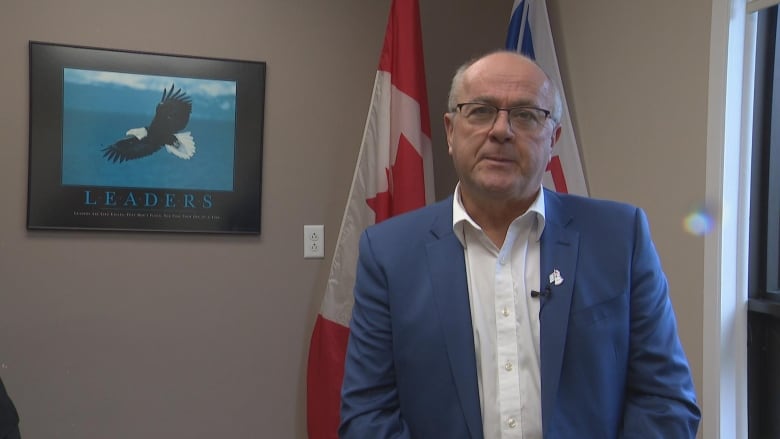 A man looks past the camera. He is wearing a blue blazer.