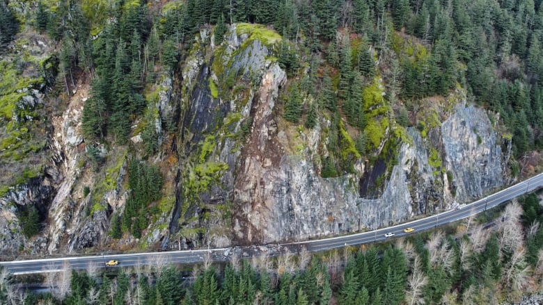 An aerial view of a blocked highway, built into a cliffside. 